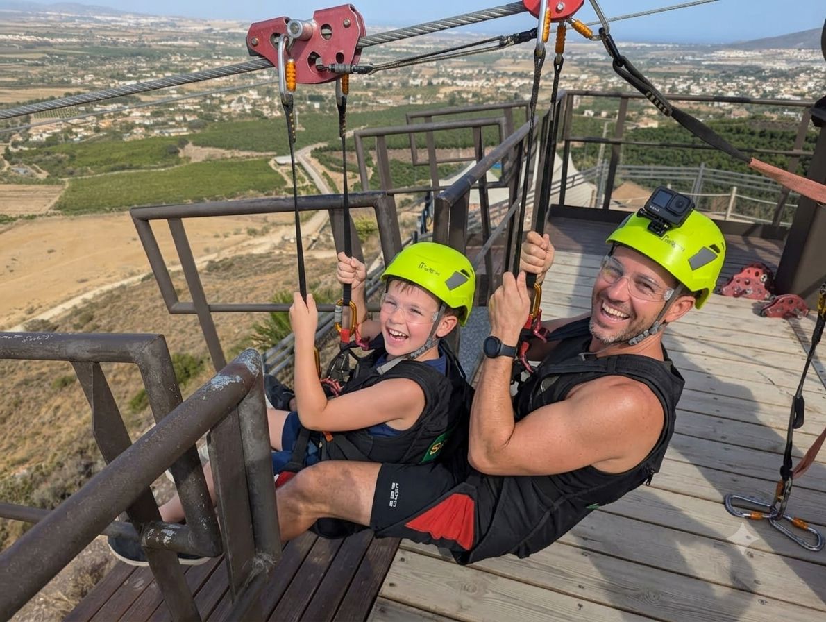 Padre e hijo sonriendo juntos en el salto en tándem de la tirolina de Sunview Park, Málaga